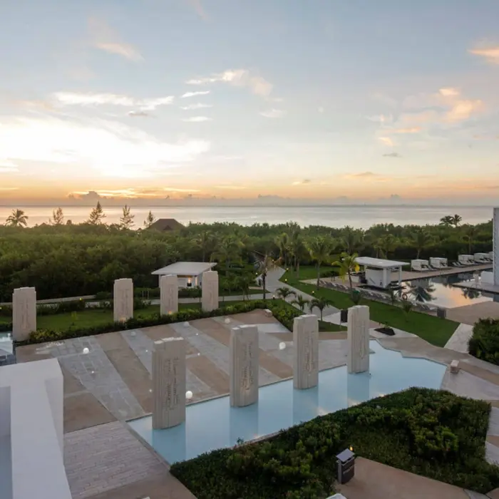 Sunset view from the rooftop, showing a decorative water feature, surrounding foliage, and the ocean in the distance.