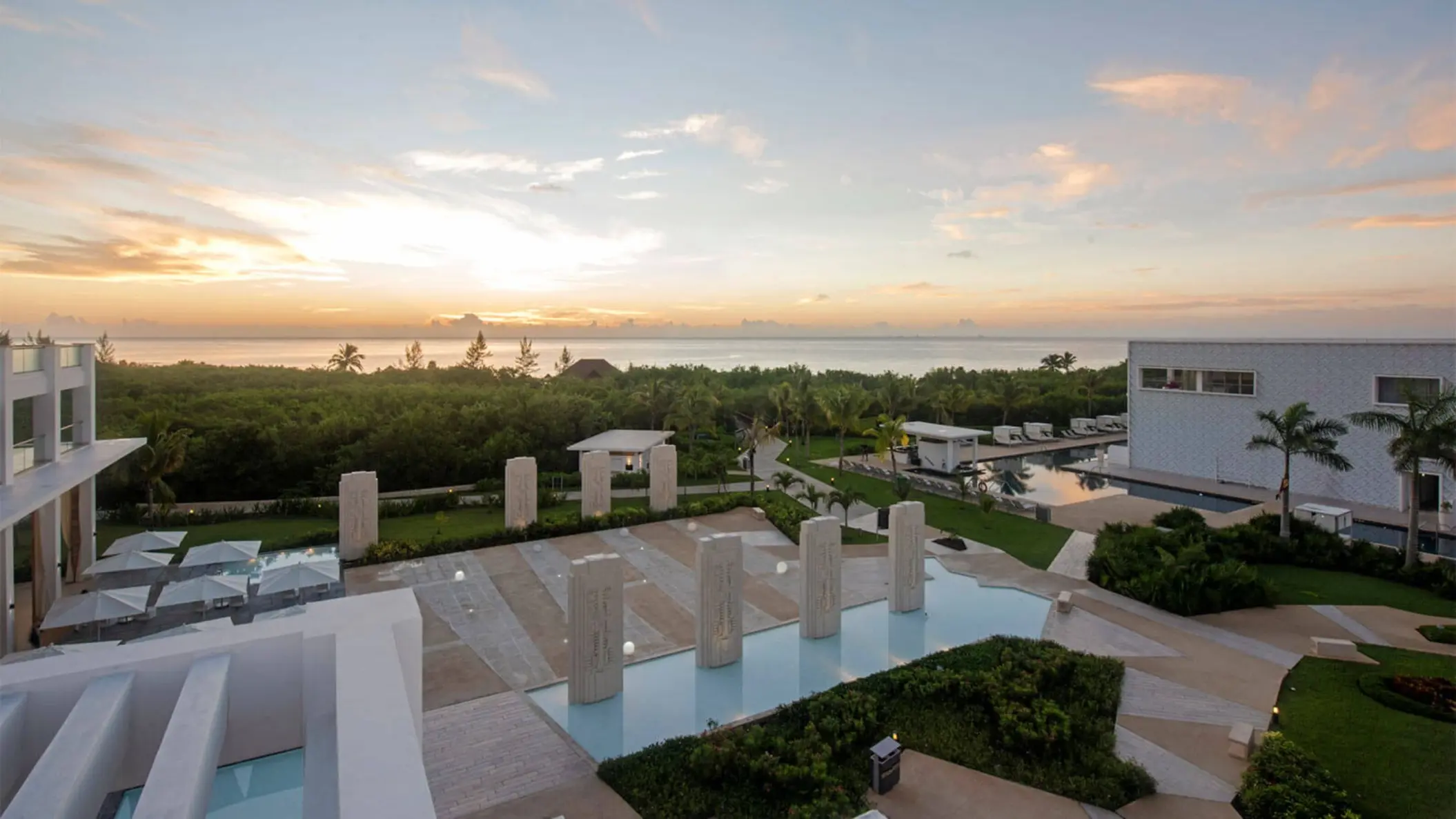 Sunset view from the rooftop, showing a decorative water feature, surrounding foliage, and the ocean in the distance.