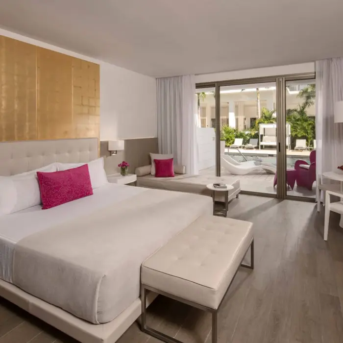Interior of a swim-up suite with a king bed, modern decor, and direct access to the pool area through a glass door.
