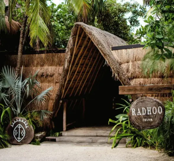 Tropical entrance to Radhoo Tulum with wooden details and lush greenery creating a boutique jungle vibe.
