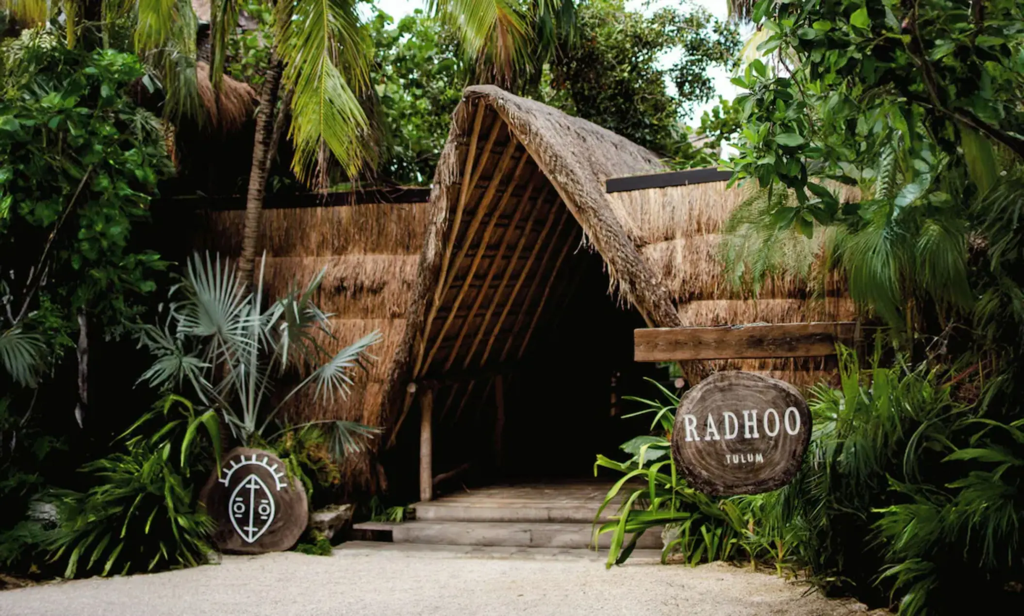 Tropical entrance to Radhoo Tulum with wooden details and lush greenery creating a boutique jungle vibe.