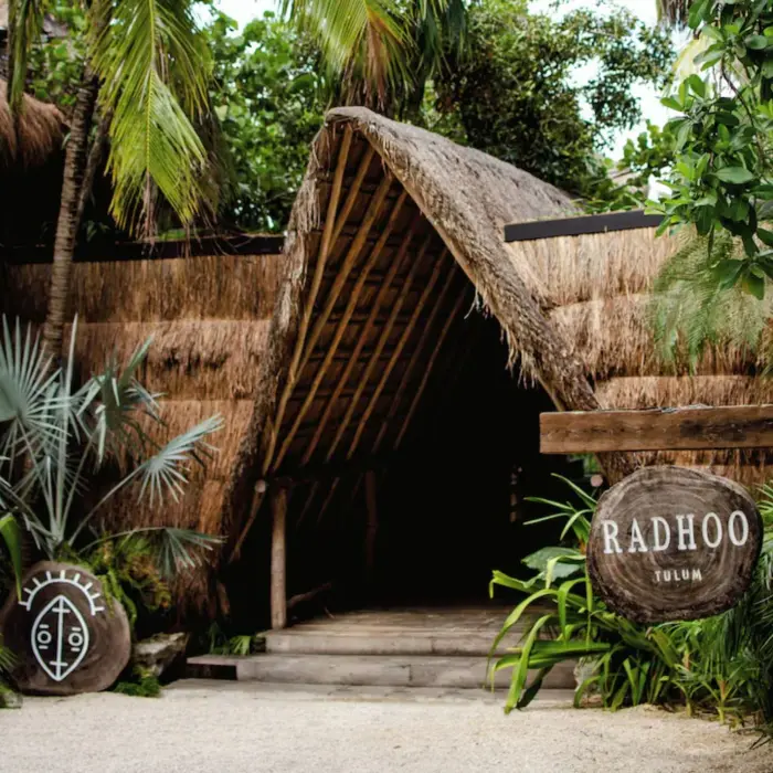 Tropical entrance to Radhoo Tulum with wooden details and lush greenery creating a boutique jungle vibe.