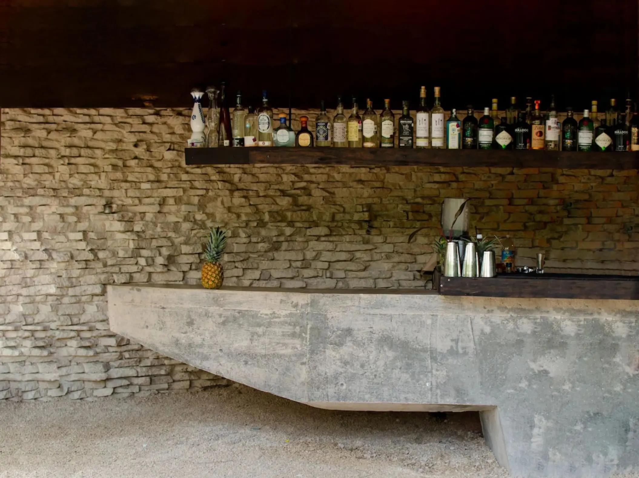 Rustic bar counter at Radhoo Tulum with warm lighting and artisanal bottles on wooden display shelves.