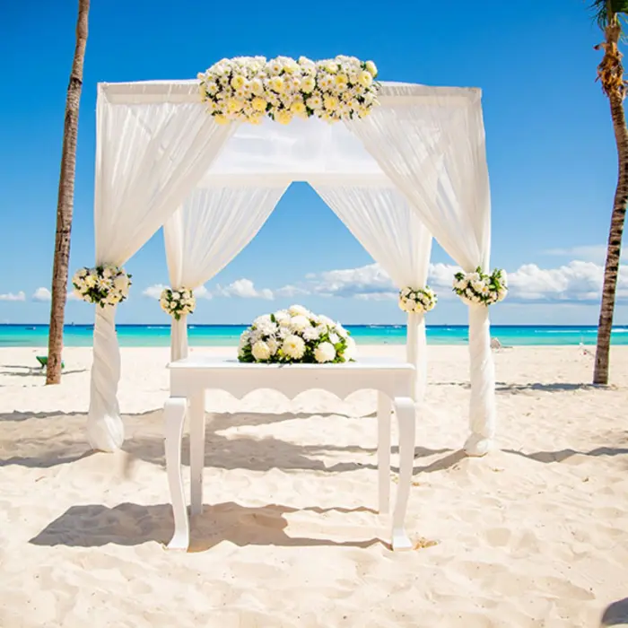 A white wedding gazebo on a pristine beach, with the turquoise ocean and palm trees in the background.