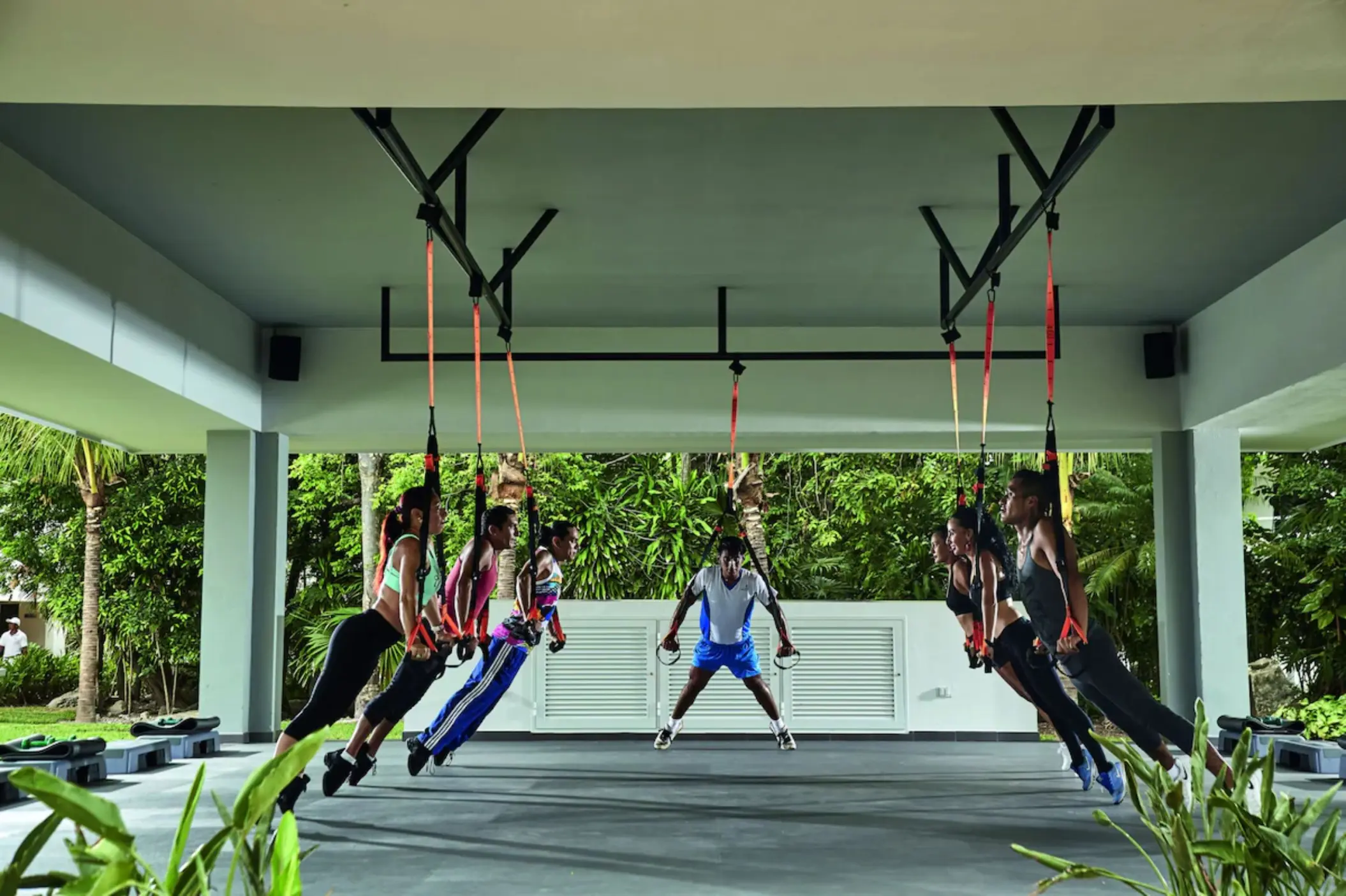 An outdoor covered fitness area where people are doing suspension training exercises.