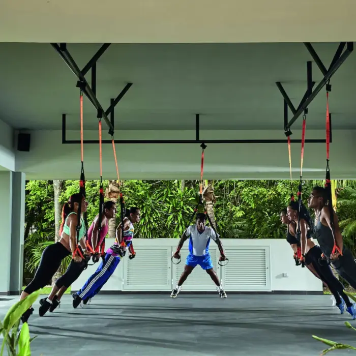An outdoor covered fitness area where people are doing suspension training exercises.