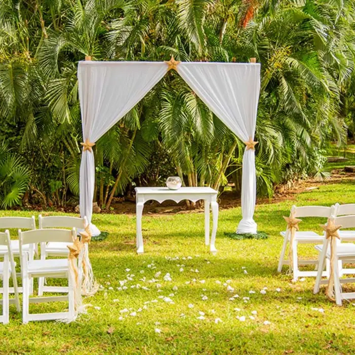 A beautiful garden wedding setup with a white gazebo, folding chairs, and scattered rose petals.