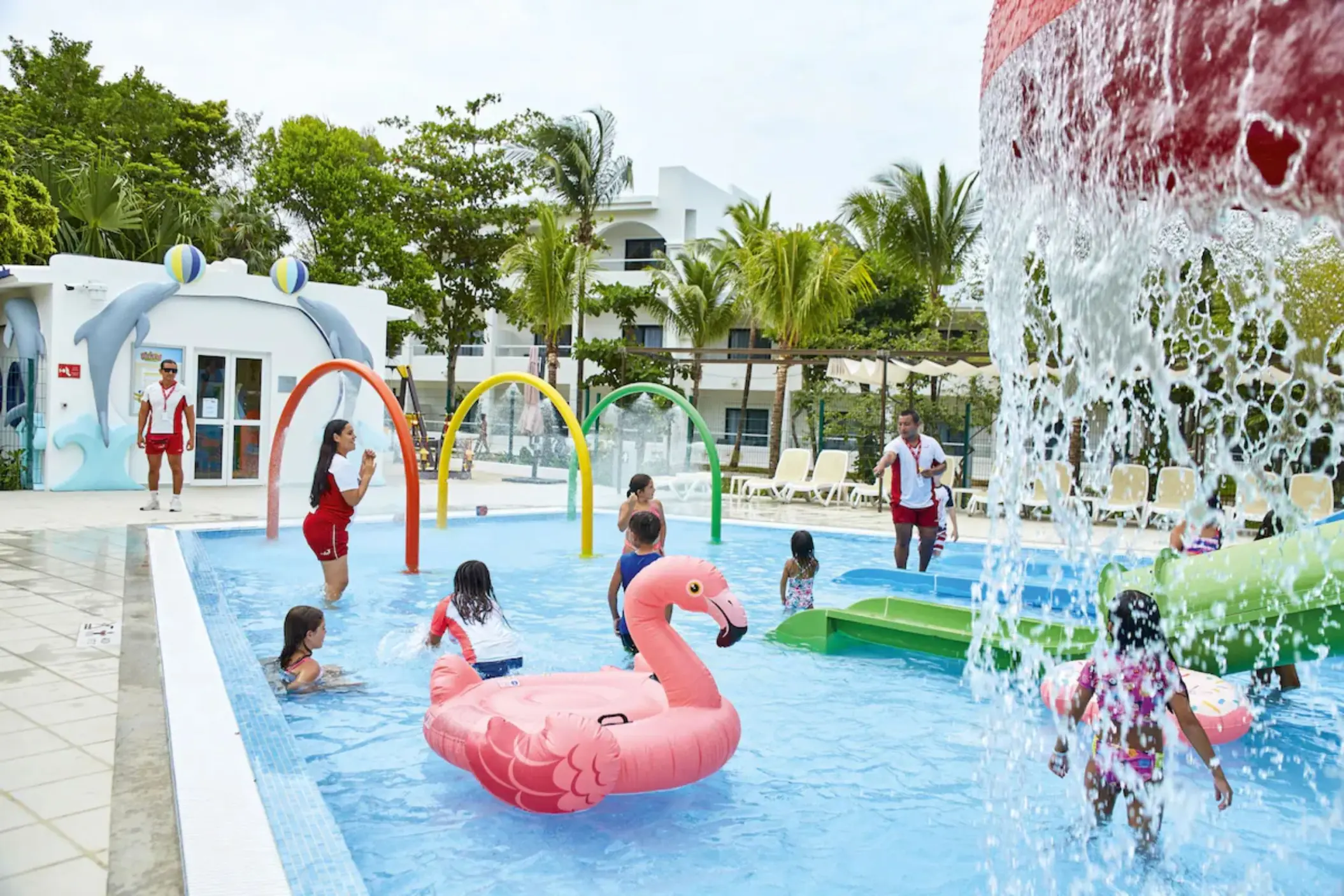 A vibrant kids' water park with slides, water features, and a large pink flamingo float in a pool.