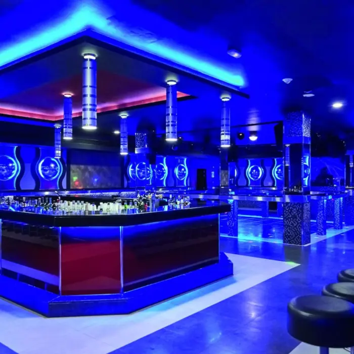 A modern, futuristic nightclub with blue lighting, a central bar, and lounge seating.