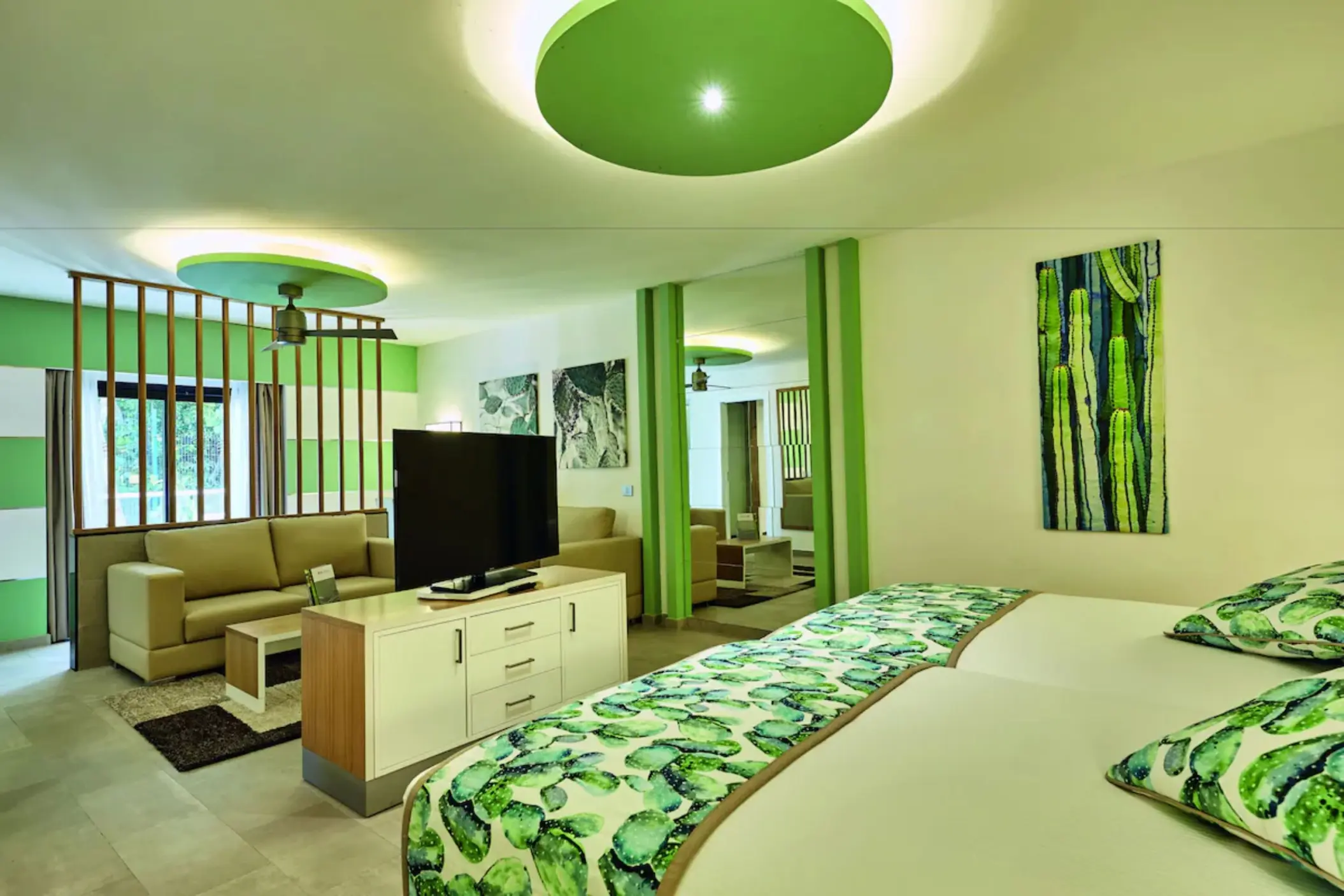 A spacious and bright suite with a bed and a separate living area with green accents and cactus art.