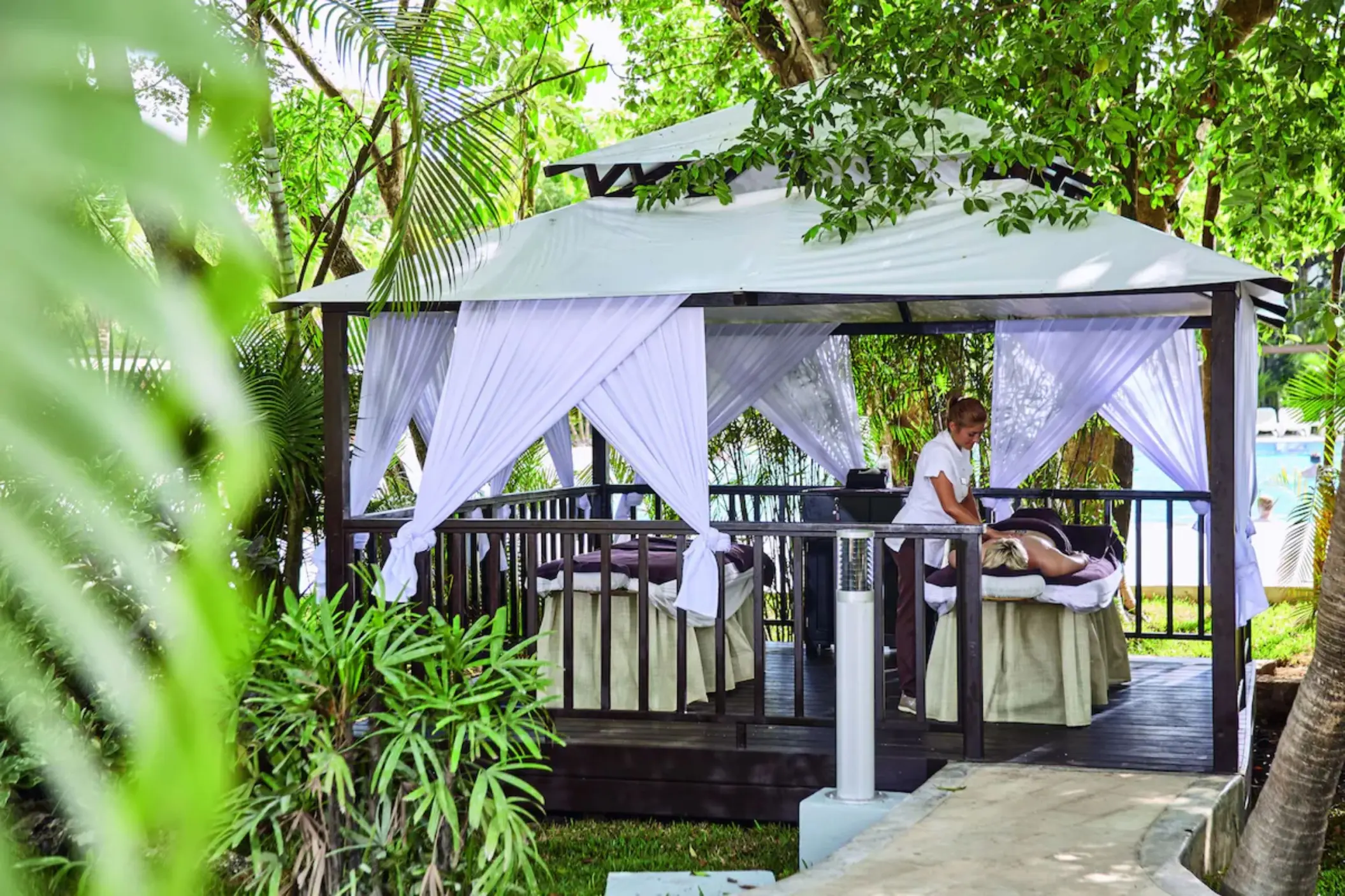 A massage therapist working on a client in a private, covered outdoor hut surrounded by lush greenery.