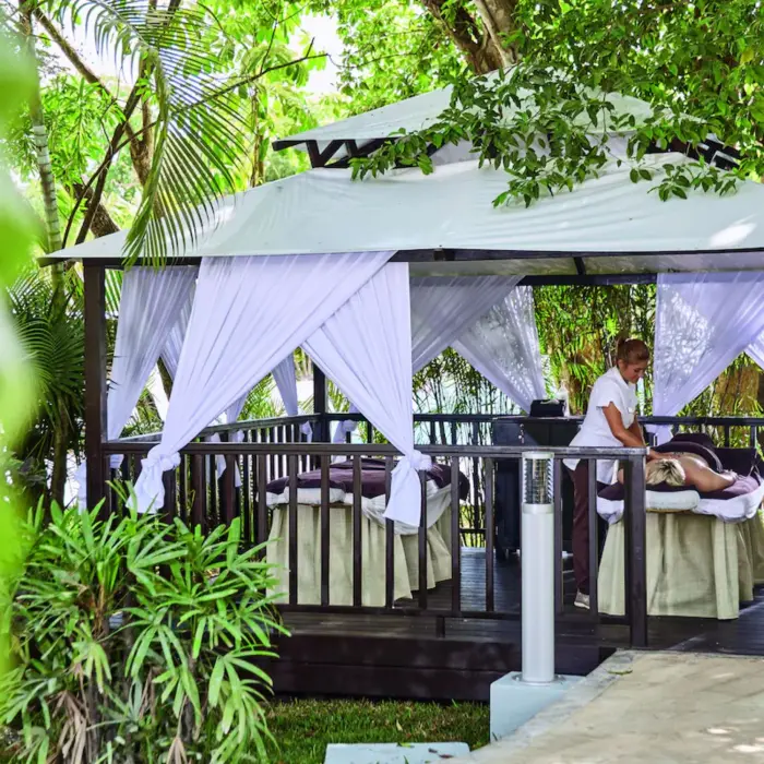 A massage therapist working on a client in a private, covered outdoor hut surrounded by lush greenery.