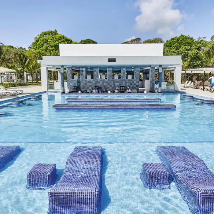 A large swimming pool with a central swim-up bar and guests enjoying the water.