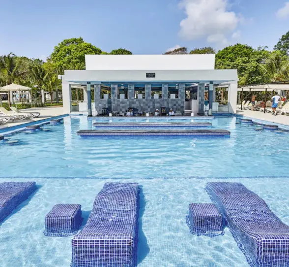 A large swimming pool with a central swim-up bar and guests enjoying the water.