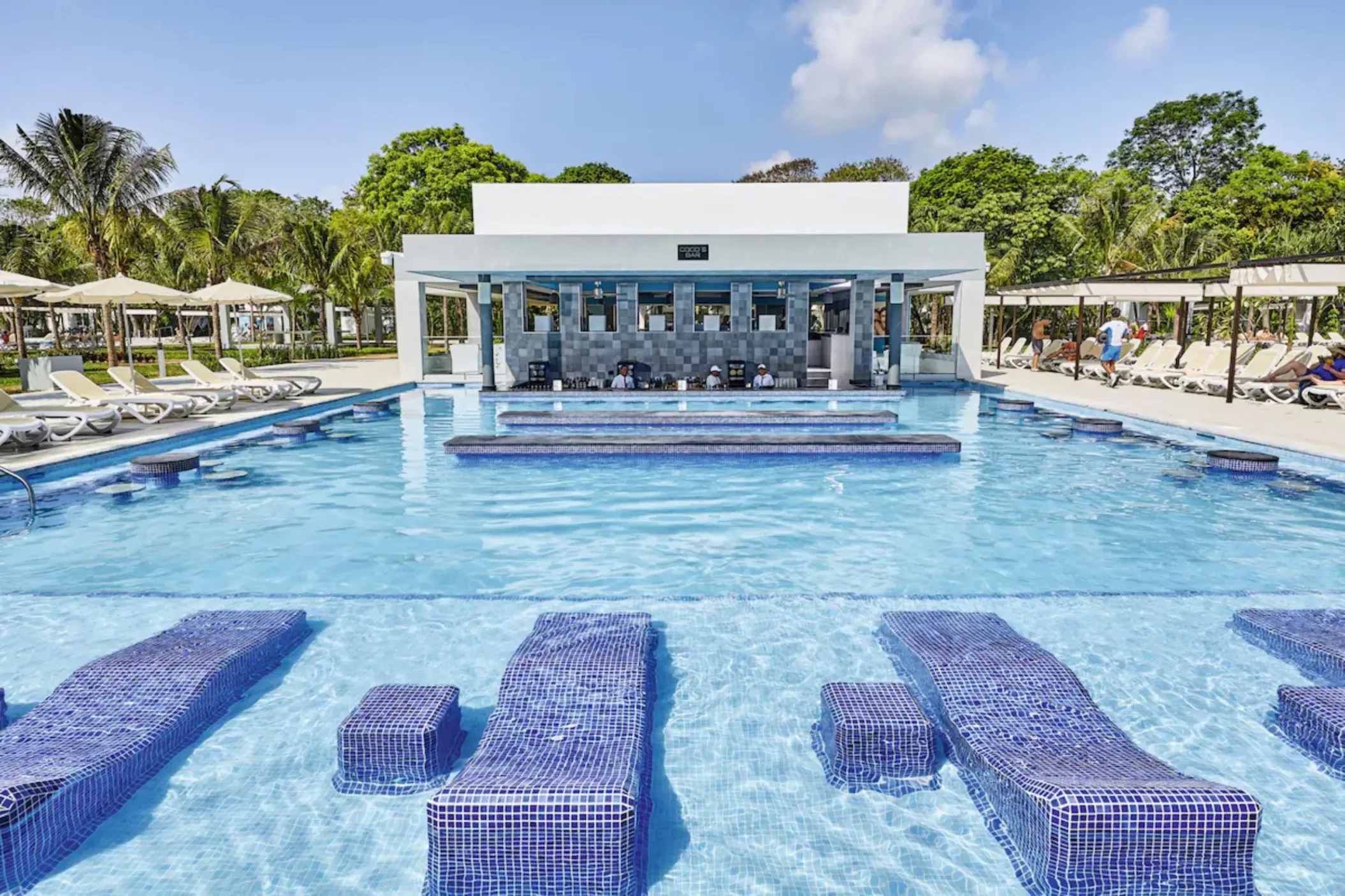 A large swimming pool with a central swim-up bar and guests enjoying the water.