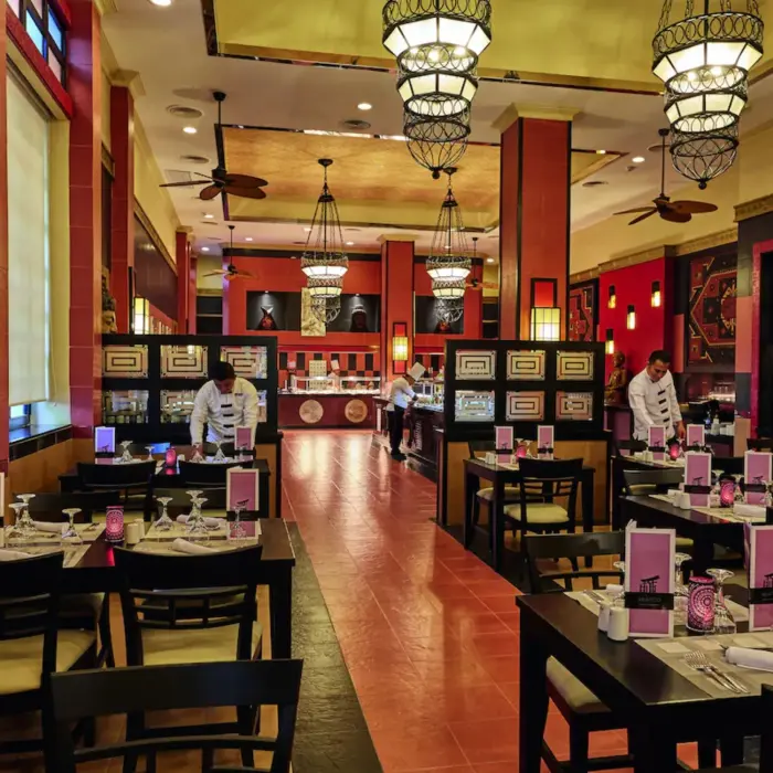 An Asian restaurant with a sushi bar, red and black decor, and tables set for dining.