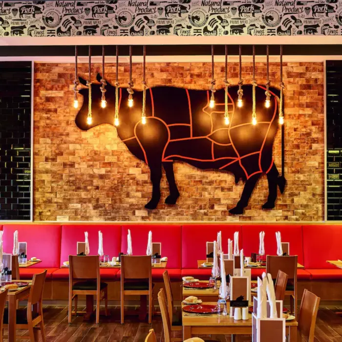 A steakhouse with dark wood tables, upholstered chairs, and a bar area.
