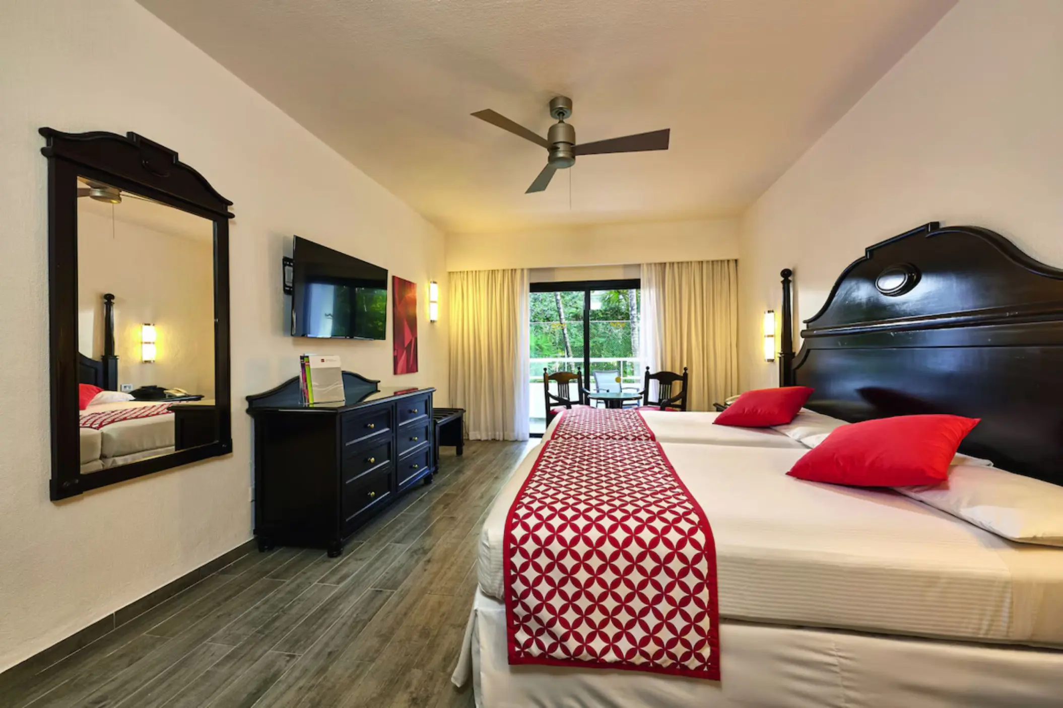 A suite with a large bed, a couch, a balcony with a garden view, and two chairs.