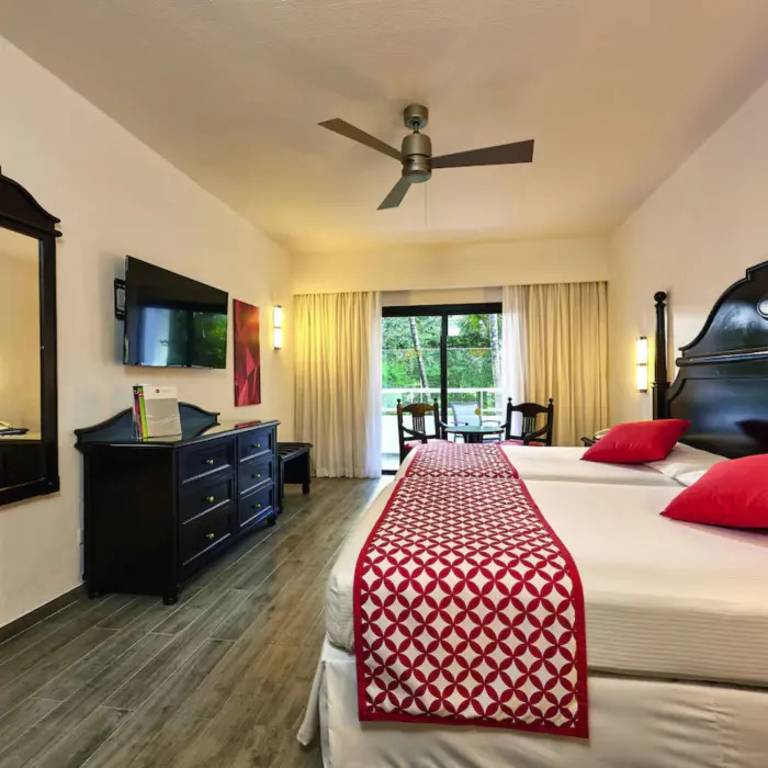 A suite with a large bed, a couch, a balcony with a garden view, and two chairs.