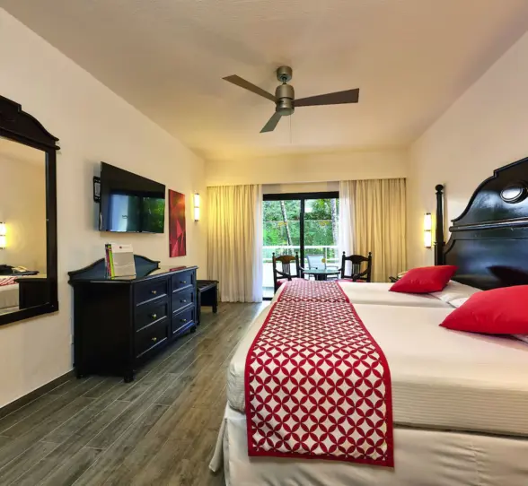 A suite with a large bed, a couch, a balcony with a garden view, and two chairs.