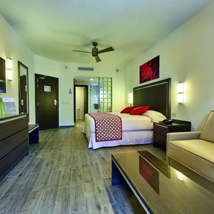 A suite with a large king-sized bed, a sofa, a mirror, and green accents.