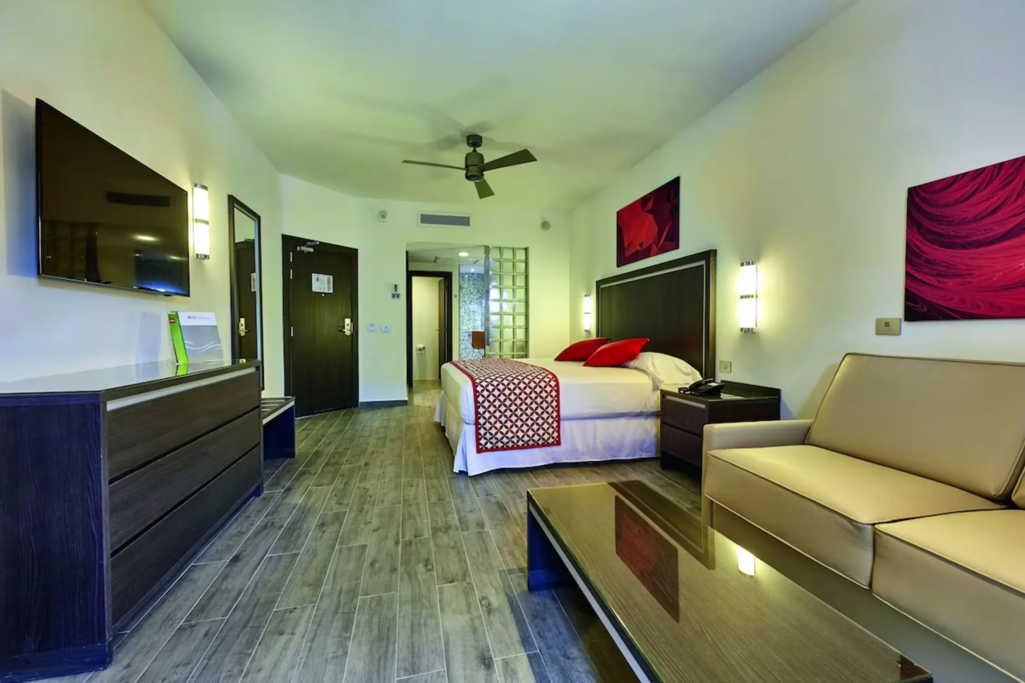 A suite with a large king-sized bed, a sofa, a mirror, and green accents.