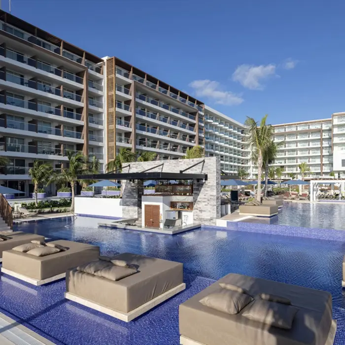 Large modern pool area with submerged sunbeds, swim-up bar, and high-rise resort buildings.