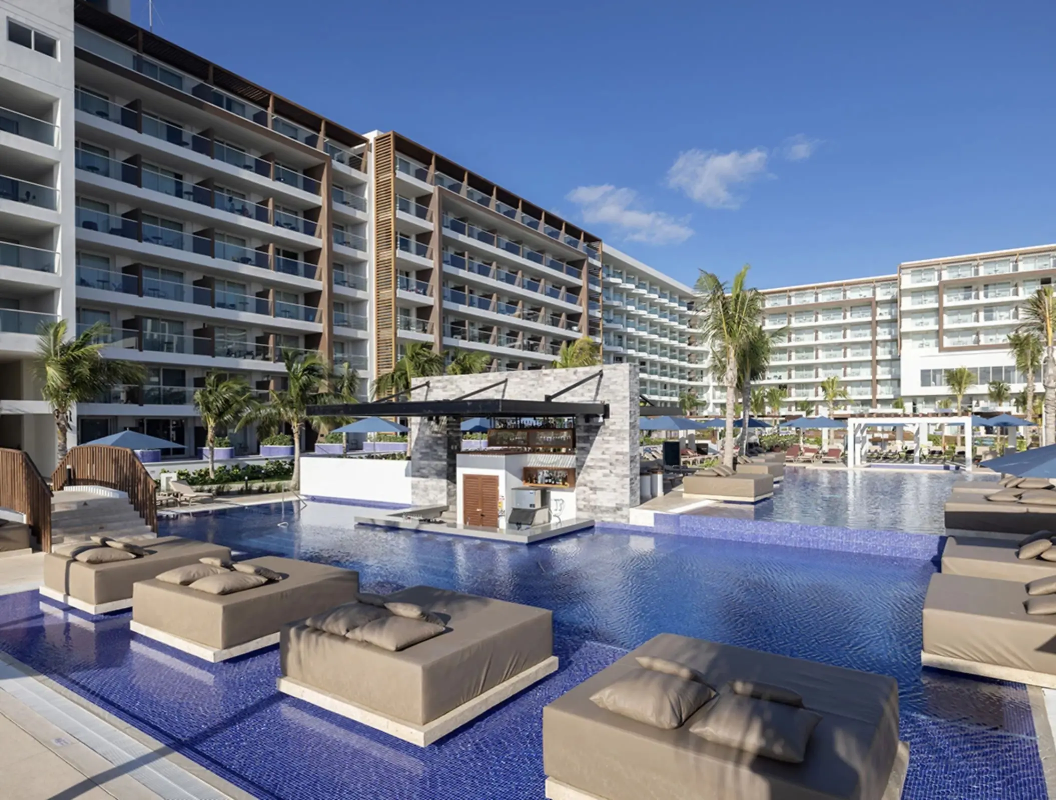 Large modern pool area with submerged sunbeds, swim-up bar, and high-rise resort buildings.