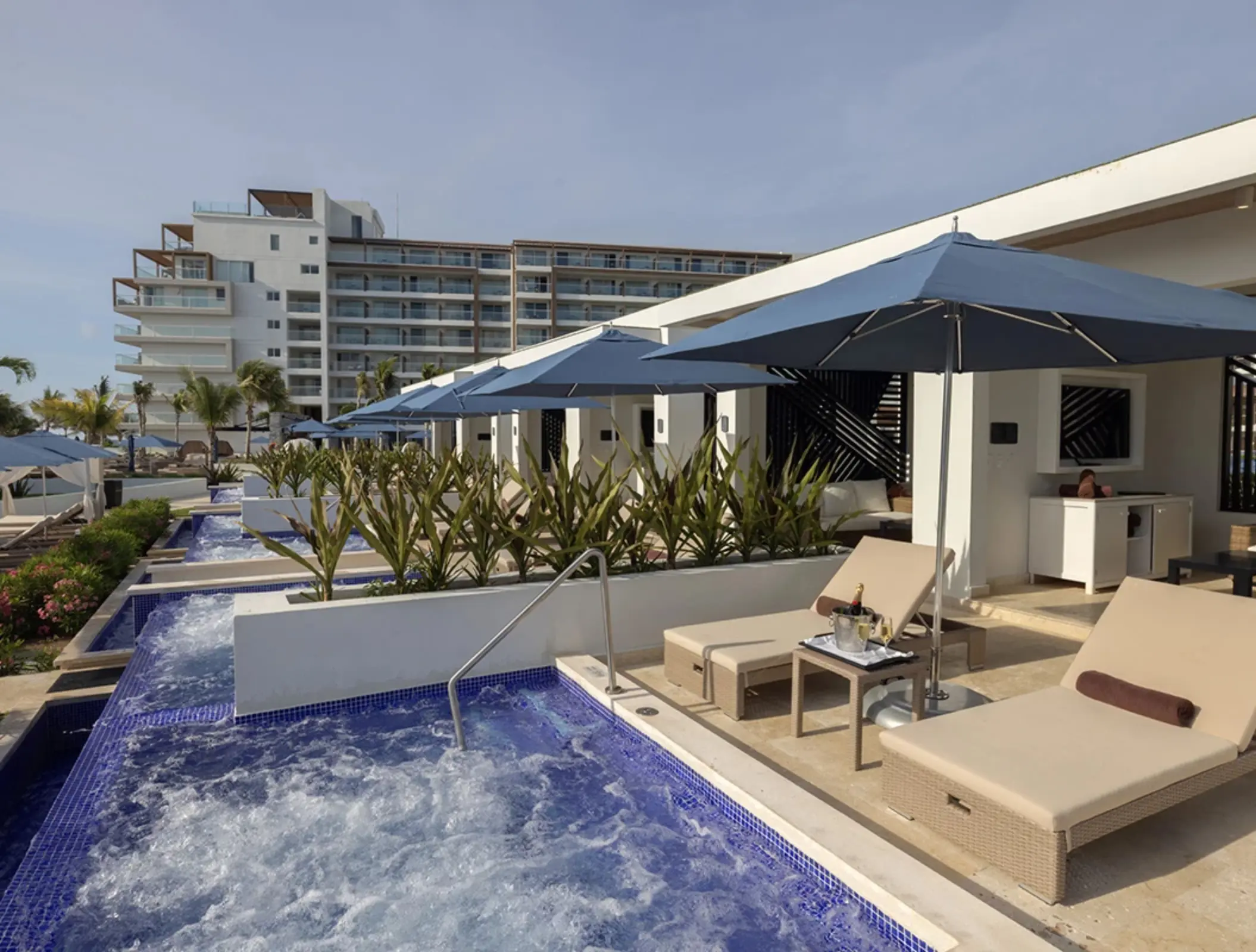 Private cabanas with lounge chairs, umbrellas, and bubbling plunge pools set in front of a luxury hotel.