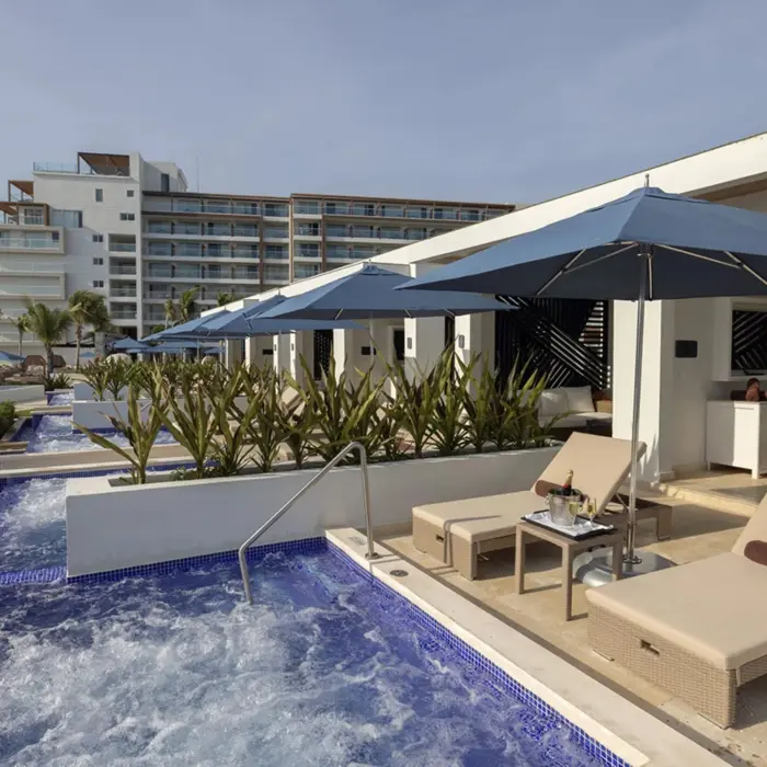 Private cabanas with lounge chairs, umbrellas, and bubbling plunge pools set in front of a luxury hotel.