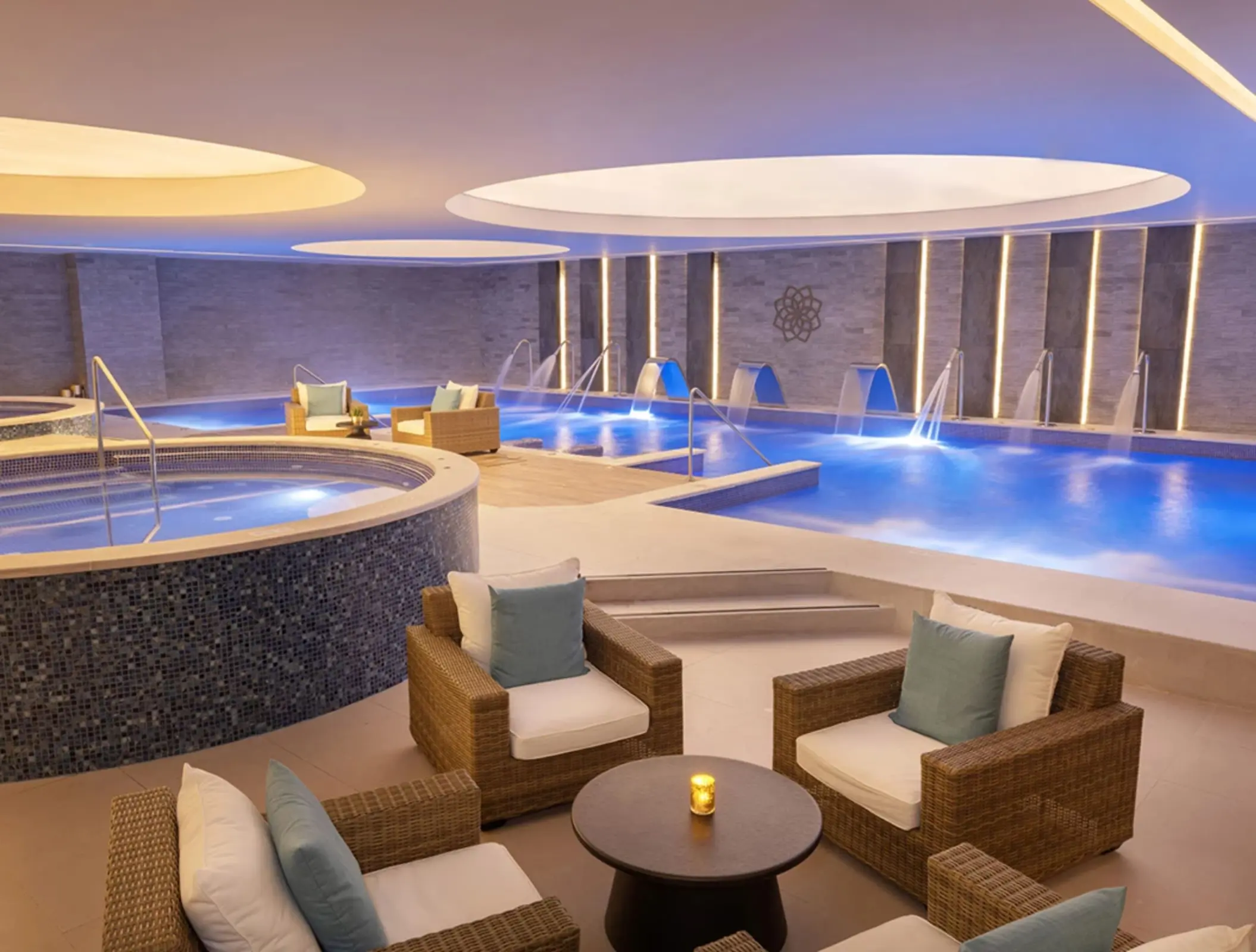 Spa hydrotherapy area with loungers, whirlpools, warm lighting, and water jets in a tranquil indoor space.