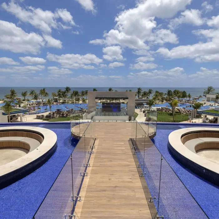 Rooftop terrace with circular hot tubs, ocean views, glass railings, and blue-tiled infinity pool.