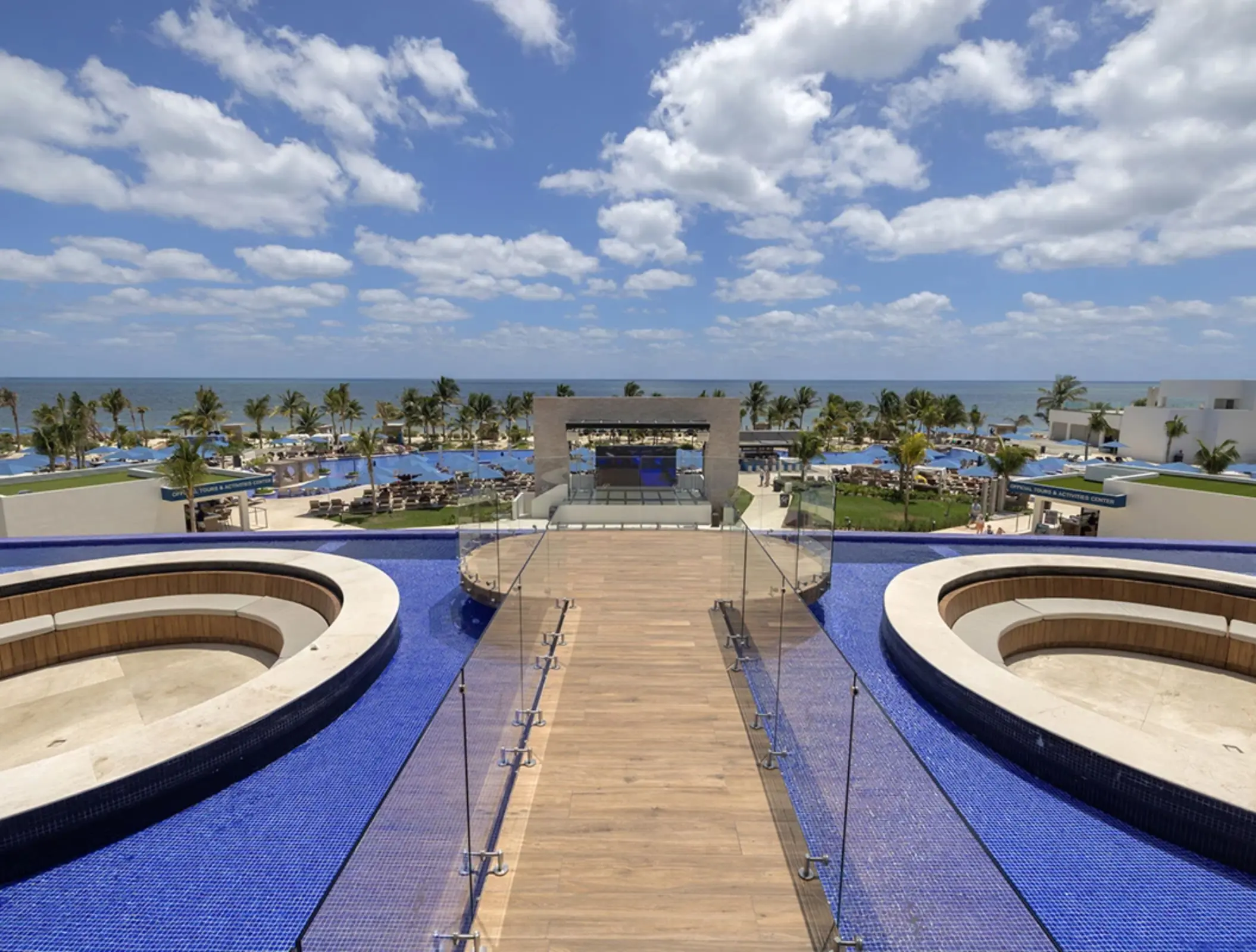Rooftop terrace with circular hot tubs, ocean views, glass railings, and blue-tiled infinity pool.