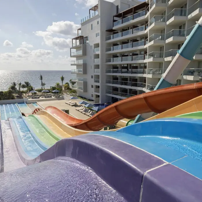 Colorful water slides with ocean views, pool loungers, and adjacent beachfront resort buildings under sunny skies.