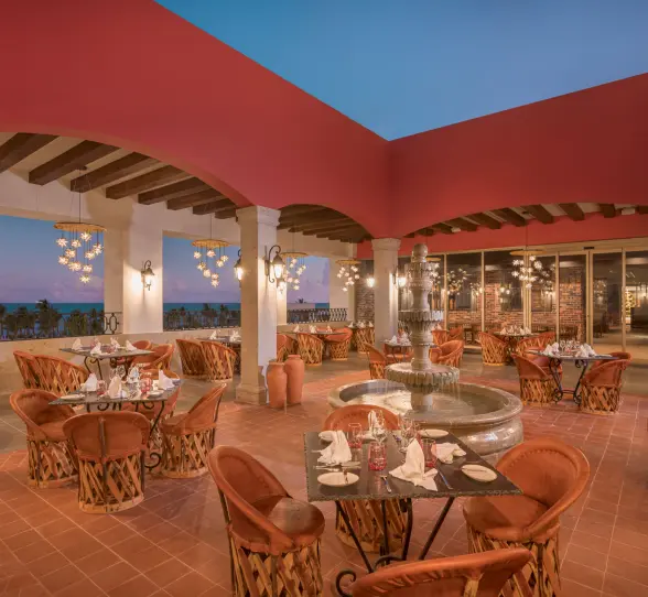 Open-air terrace restaurant with terracotta floors, Mexican decor, and ocean views at sunset.