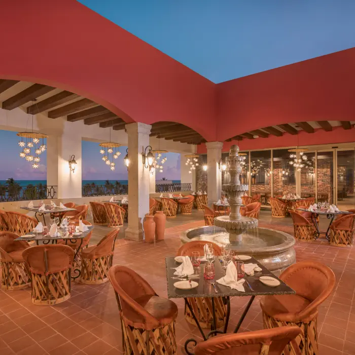Open-air terrace restaurant with terracotta floors, Mexican decor, and ocean views at sunset.