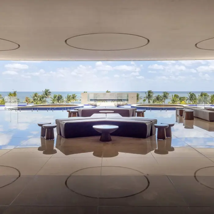 Sleek open-air lounge with ocean views, an infinity pool, and modern furniture reflecting on a polished floor.