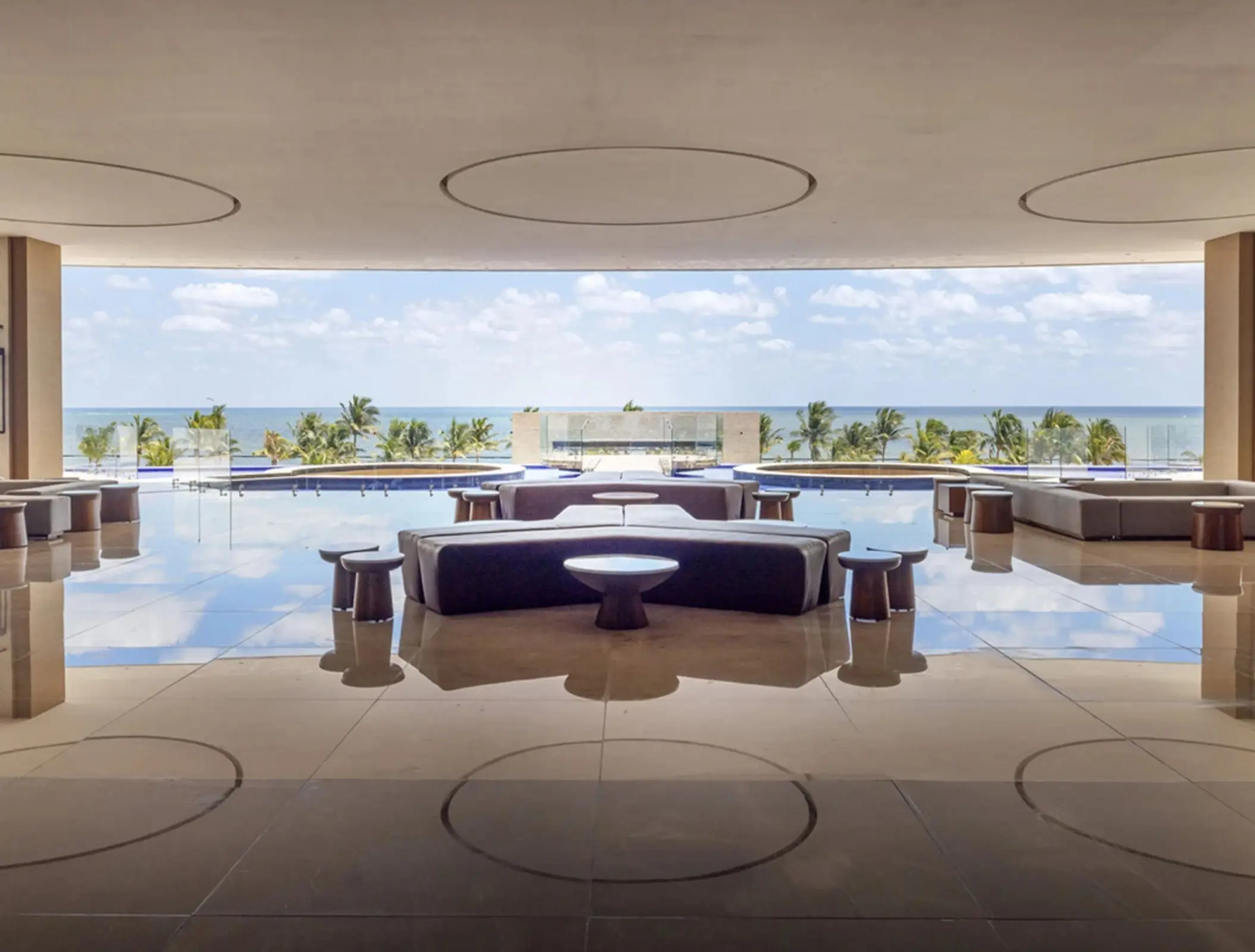 Sleek open-air lounge with ocean views, an infinity pool, and modern furniture reflecting on a polished floor.