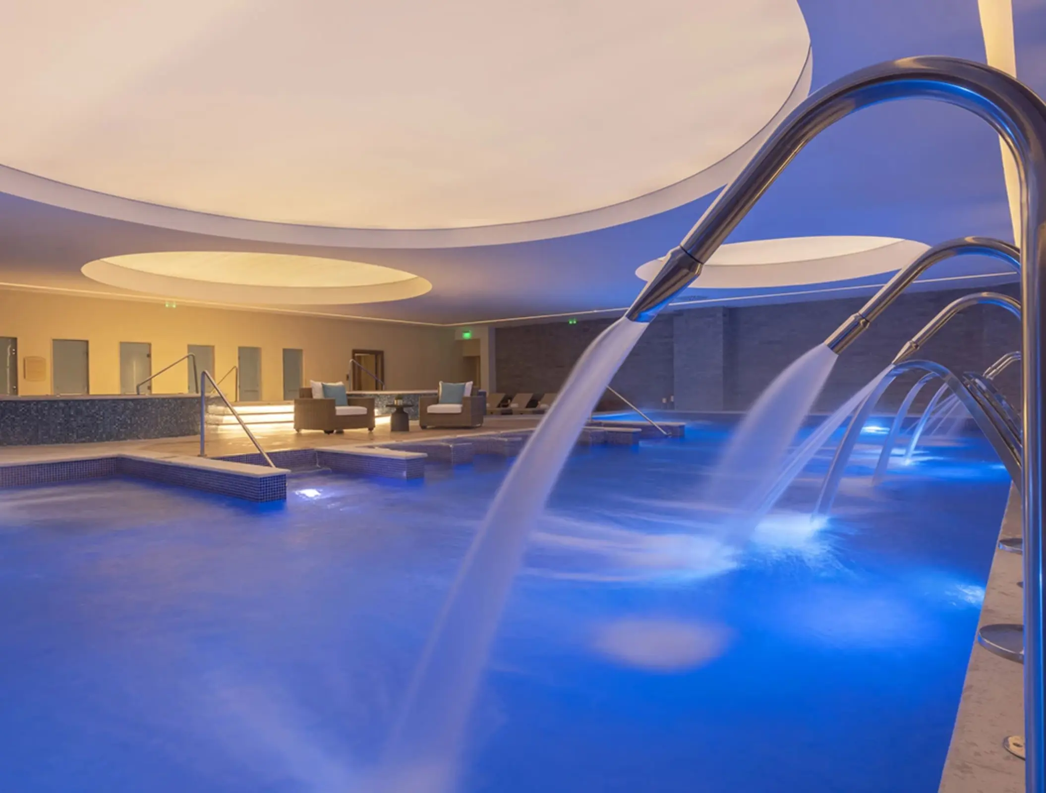 Indoor spa pool with cascading hydrotherapy jets, ambient lighting, and a circular ceiling feature for relaxation.