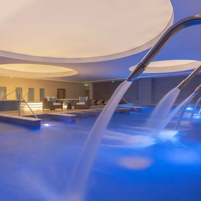 Indoor spa pool with cascading hydrotherapy jets, ambient lighting, and a circular ceiling feature for relaxation.
