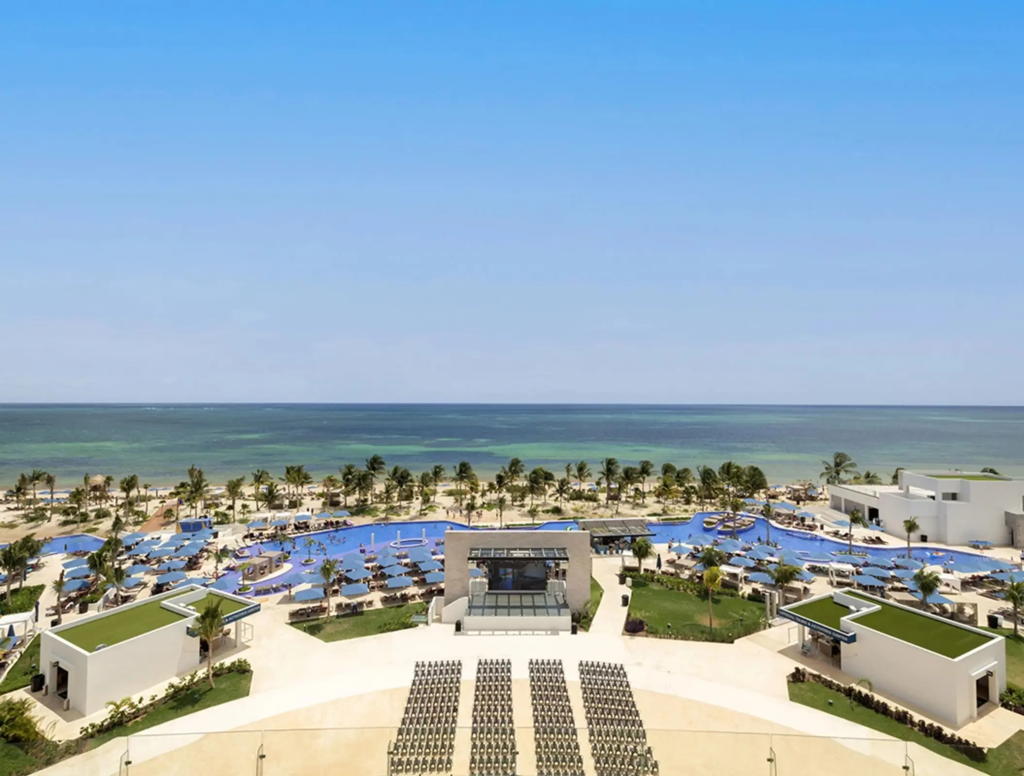 Aerial view of beachfront resort with large pools, palm trees, and sun loungers facing the turquoise Caribbean Sea.