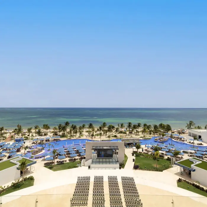 Aerial view of beachfront resort with large pools, palm trees, and sun loungers facing the turquoise Caribbean Sea.
