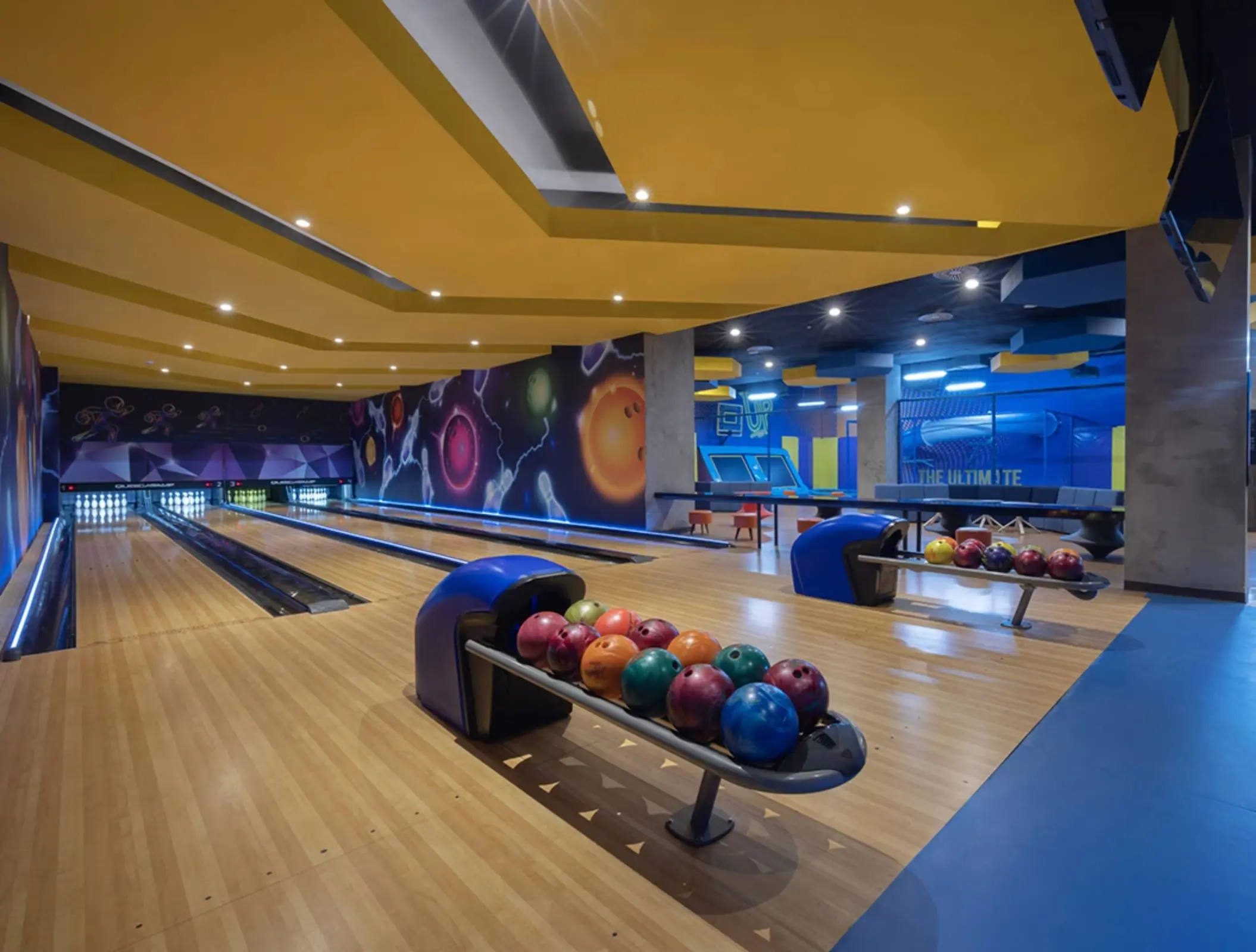 Bright, colorful bowling alley with two lanes, cosmic-themed decor, and bowling balls ready for play.