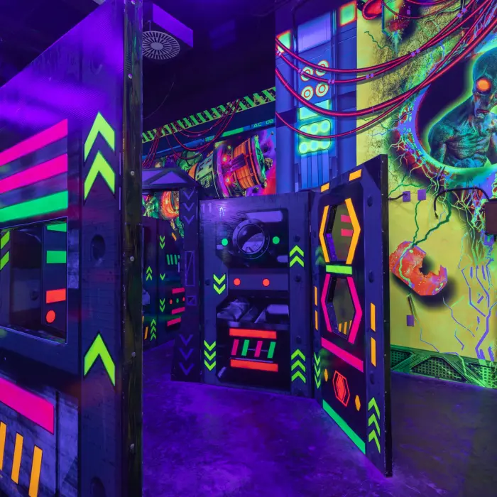 Neon-lit laser tag arena with alien-themed wall art and vibrant obstacles under blacklight for energetic play.