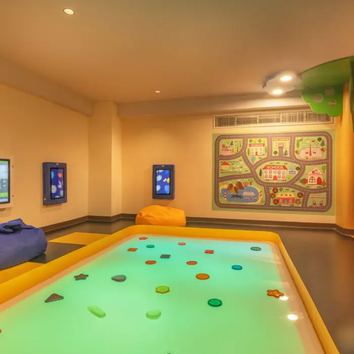 Colorful kids club with digital screens, bean bags, and an interactive floor game designed for young children.