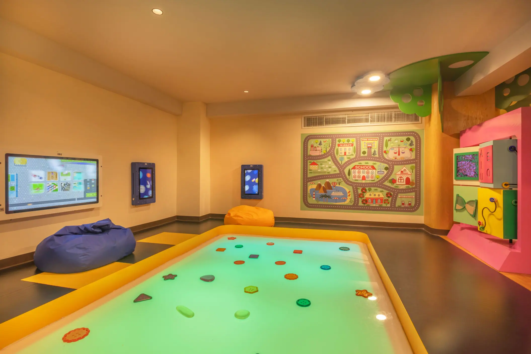 Colorful kids club with digital screens, bean bags, and an interactive floor game designed for young children.