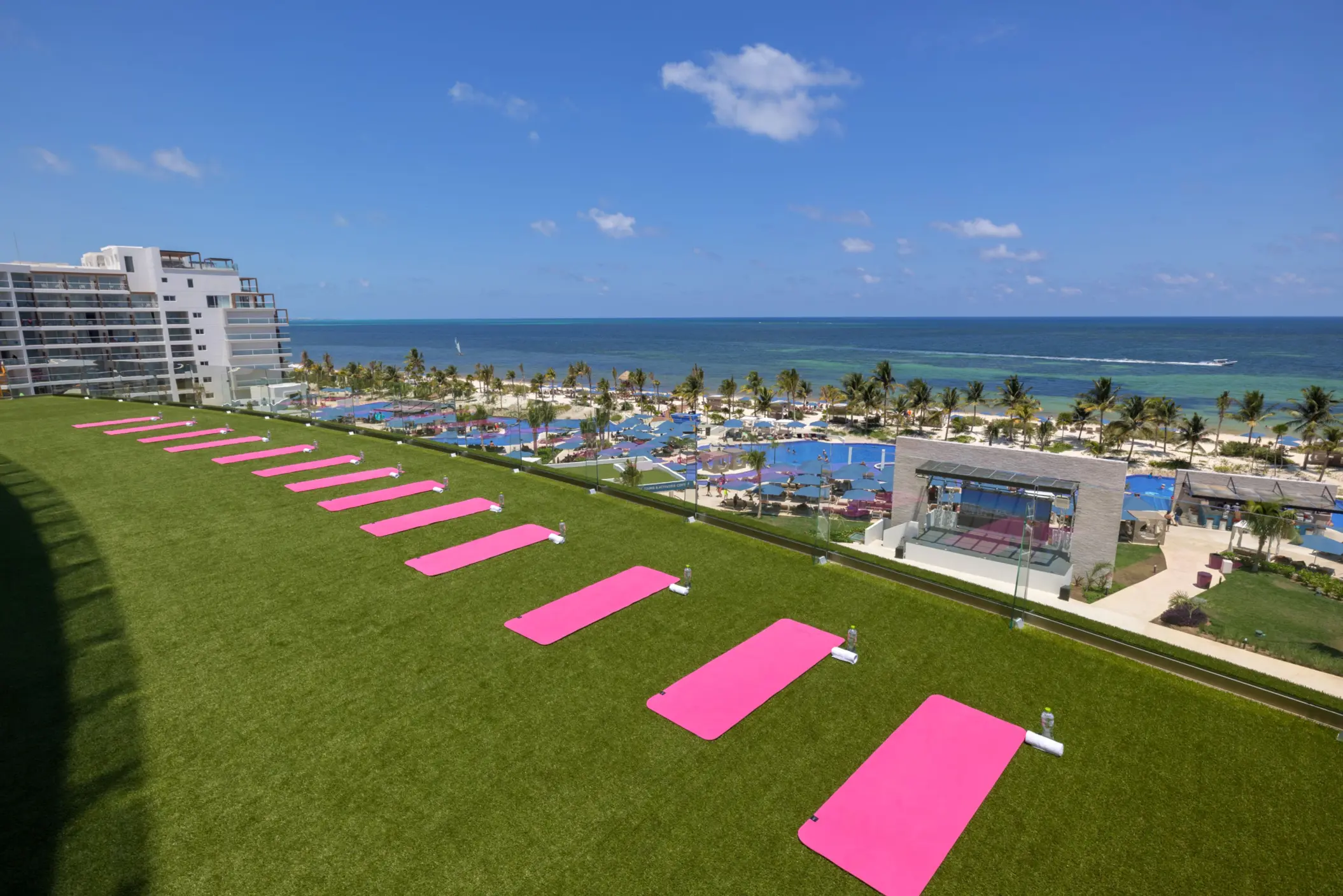 Rooftop fitness lawn with pink yoga mats facing the ocean, offering panoramic beach and resort views.