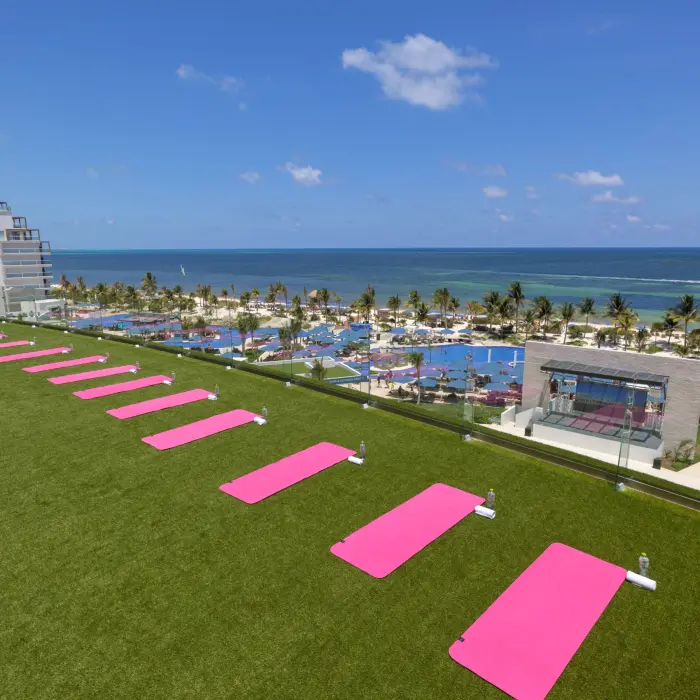 Rooftop fitness lawn with pink yoga mats facing the ocean, offering panoramic beach and resort views.