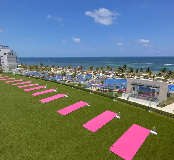 Rooftop fitness lawn with pink yoga mats facing the ocean, offering panoramic beach and resort views.