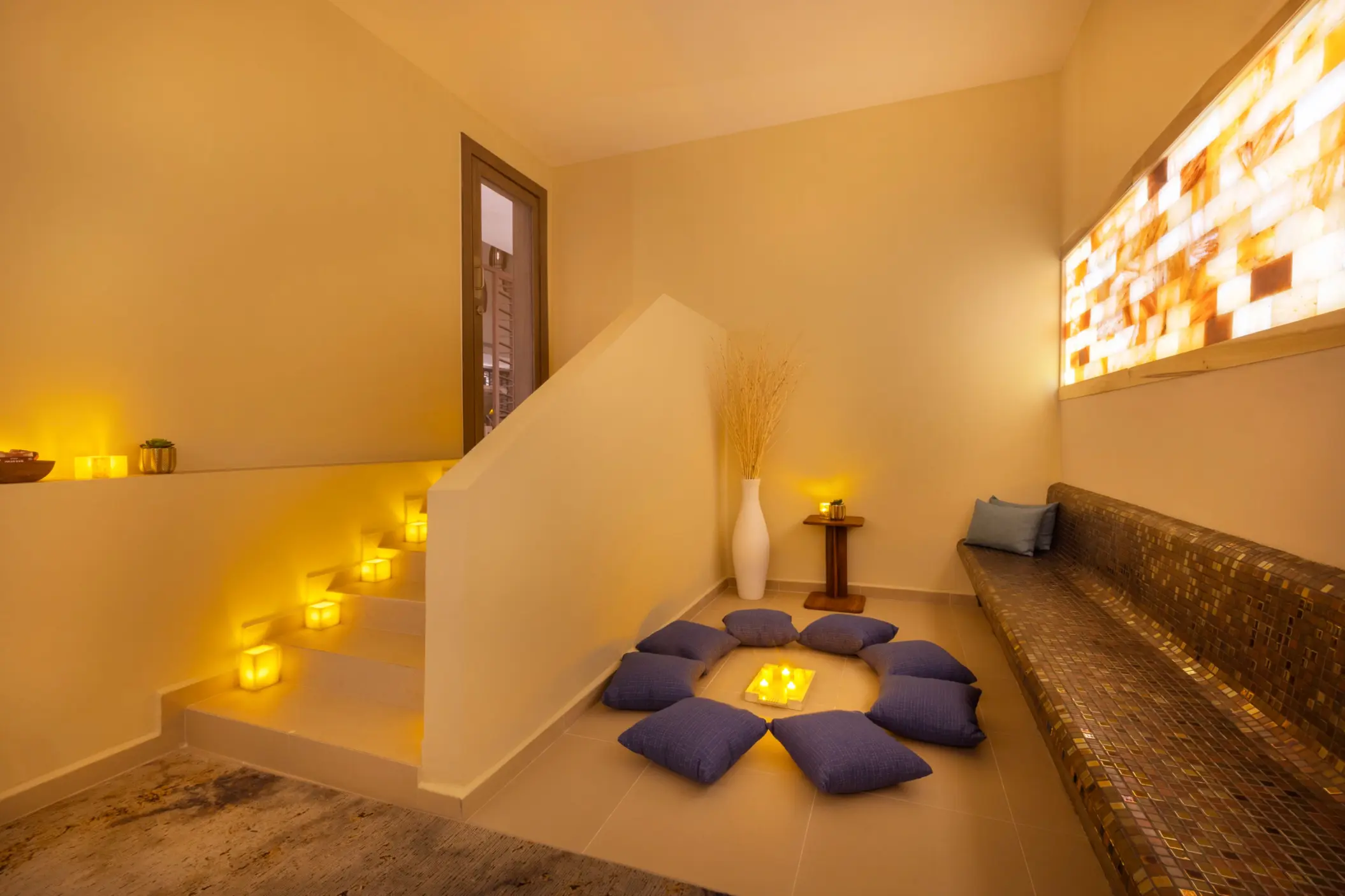 Dimly lit meditation area with circle of cushions and glowing candles for peaceful, ambient spa relaxation.